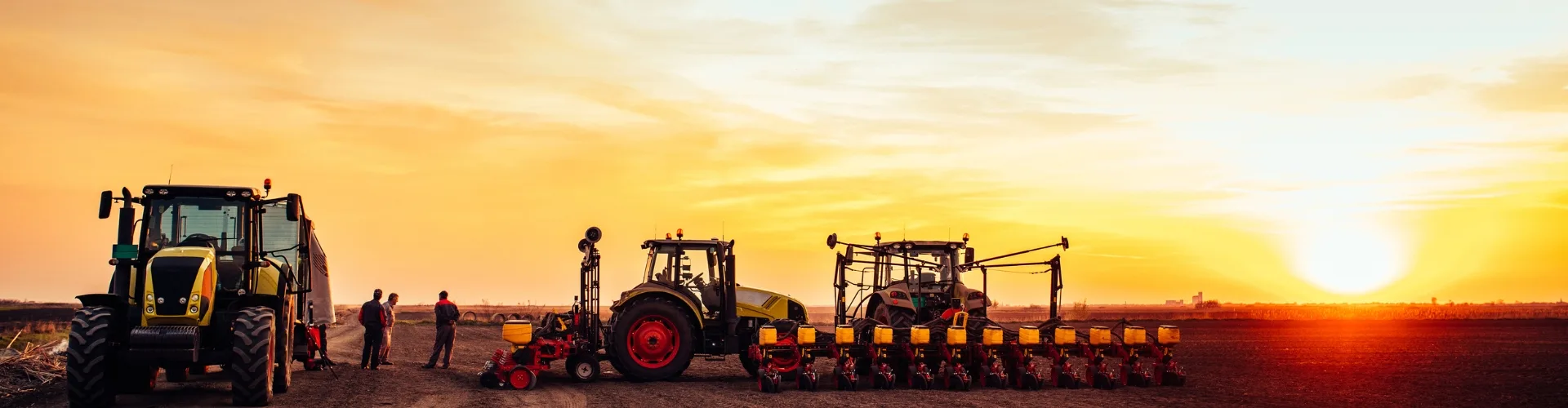 A picturesque sunset over a field with tractors and farmers preparing for planting.